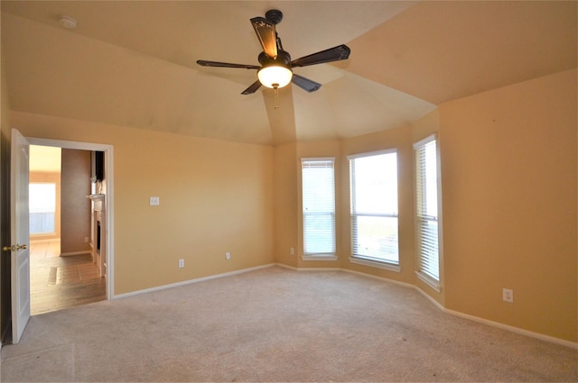 spare room featuring healthy amount of natural light, a ceiling fan, light carpet, baseboards, and vaulted ceiling