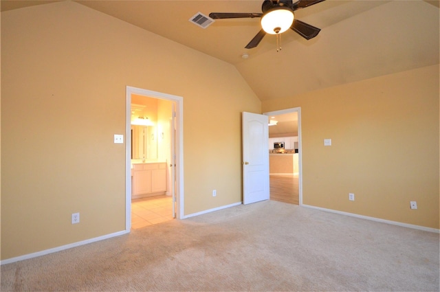 unfurnished bedroom featuring lofted ceiling, light carpet, baseboards, ensuite bath, and a ceiling fan