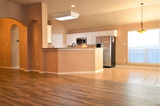 kitchen with appliances with stainless steel finishes, vaulted ceiling, wood finished floors, a peninsula, and white cabinets