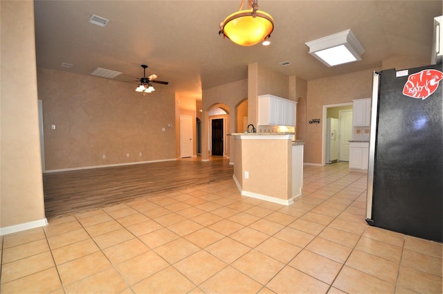 kitchen with freestanding refrigerator, arched walkways, open floor plan, white cabinetry, and a ceiling fan