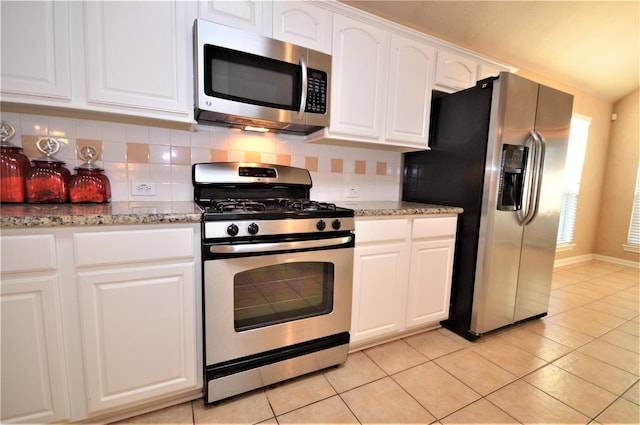kitchen with appliances with stainless steel finishes, tasteful backsplash, white cabinets, light stone counters, and light tile patterned floors