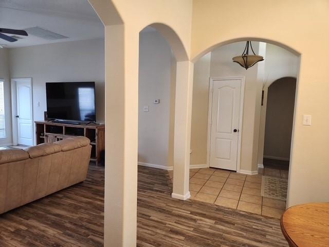 living area with dark wood-type flooring, a ceiling fan, arched walkways, and baseboards