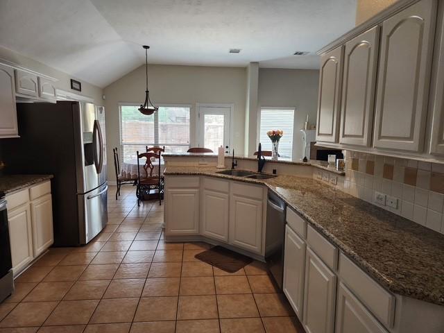 kitchen with a sink, appliances with stainless steel finishes, a peninsula, backsplash, and vaulted ceiling