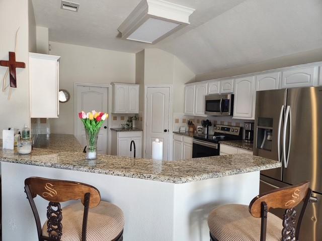 kitchen with appliances with stainless steel finishes, a peninsula, a kitchen breakfast bar, lofted ceiling, and tasteful backsplash