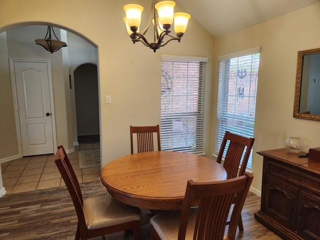 dining space with arched walkways, a chandelier, lofted ceiling, light wood-style flooring, and baseboards