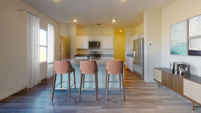 21631 Cottage Ln, New Caney, TX 77357 - kitchen with appliances with stainless steel finishes, white cabinets, an island with sink, light wood finished floors, and recessed lighting