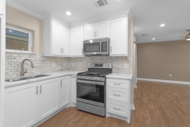 kitchen featuring appliances with stainless steel finishes, a sink, ceiling fan, light wood-style flooring, and backsplash