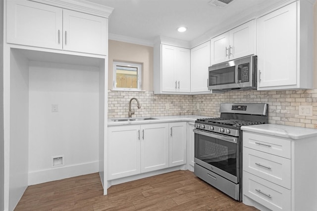 kitchen featuring appliances with stainless steel finishes, a sink, tasteful backsplash, light wood-type flooring, and white cabinetry
