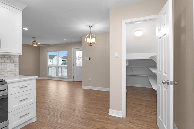 kitchen featuring baseboards, light countertops, white cabinets, light wood finished floors, and ceiling fan
