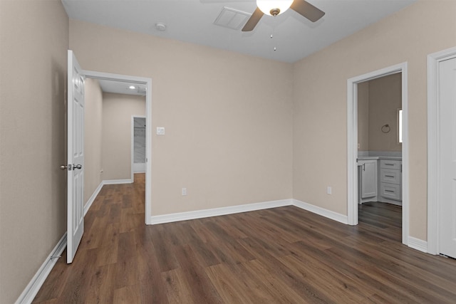 unfurnished bedroom featuring dark wood-style floors, baseboards, ensuite bathroom, and a ceiling fan
