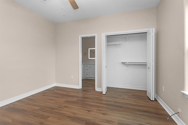 unfurnished bedroom with wood finished floors, a closet, baseboards, and ensuite bath