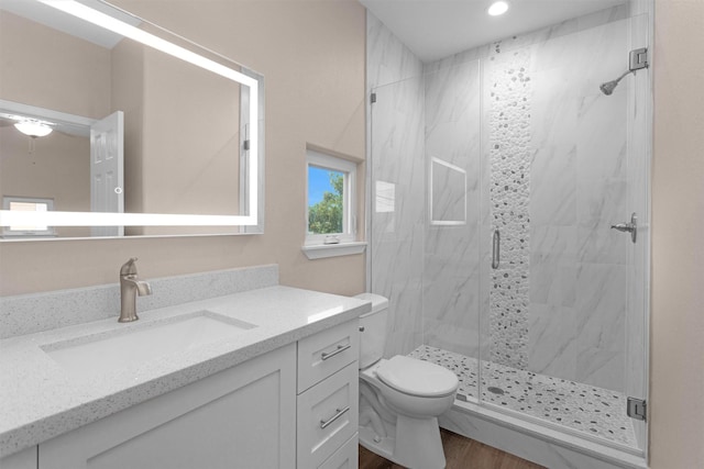 bathroom featuring toilet, a marble finish shower, vanity, wood finished floors, and recessed lighting