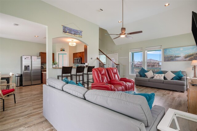 living room with arched walkways, light wood-style flooring, ceiling fan, stairway, and recessed lighting