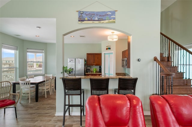 dining space featuring wood finished floors, arched walkways, stairway, and baseboards