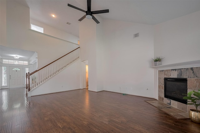 unfurnished living room with high vaulted ceiling, stairway, wood finished floors, a tile fireplace, and ceiling fan