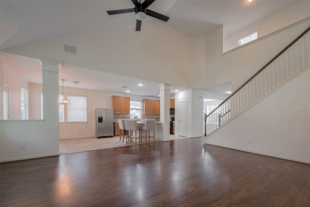 living area with decorative columns, light wood-type flooring, ceiling fan, baseboards, and high vaulted ceiling