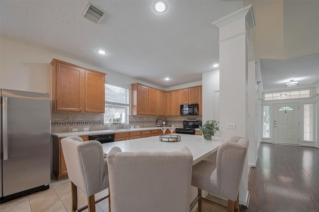 kitchen featuring black appliances, a sink, light countertops, decorative backsplash, and a textured ceiling