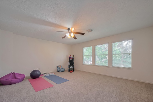 exercise area with a ceiling fan, carpet, baseboards, and a textured ceiling