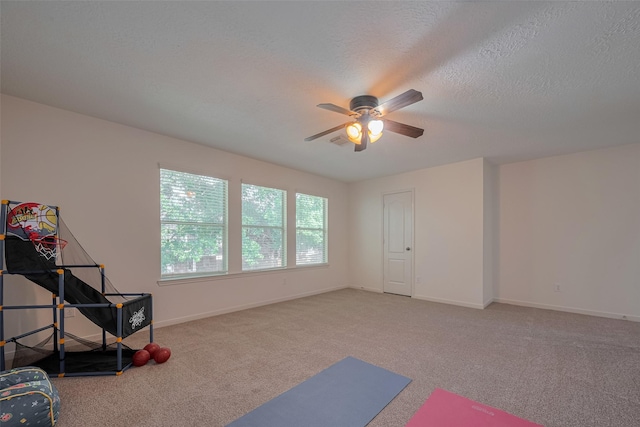 exercise room with carpet floors, a ceiling fan, baseboards, and a textured ceiling