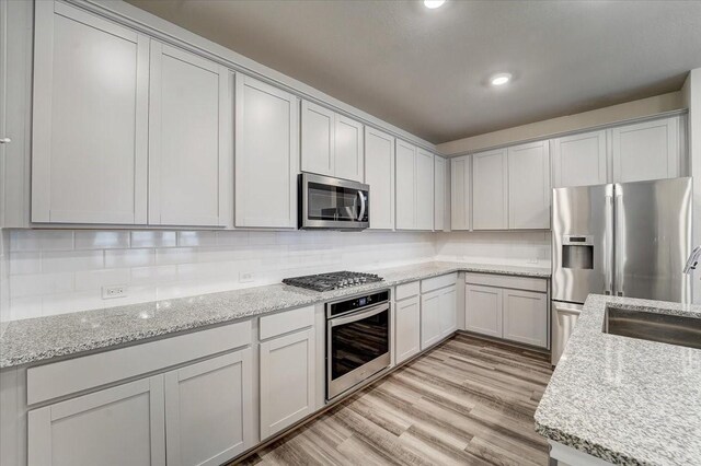 9438 Caddo Ridge Ln, Cypress, TX 77433 - kitchen featuring appliances with stainless steel finishes, light wood-style floors, a sink, tasteful backsplash, and light stone countertops