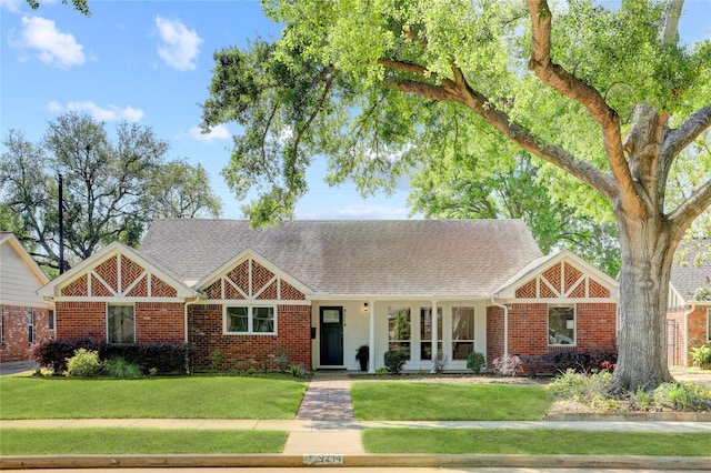 view of front facade with a front lawn, brick siding, and roof with shingles