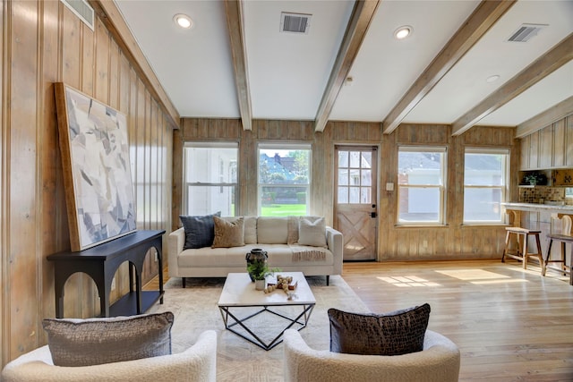 living room featuring wood walls, light wood-type flooring, and beam ceiling