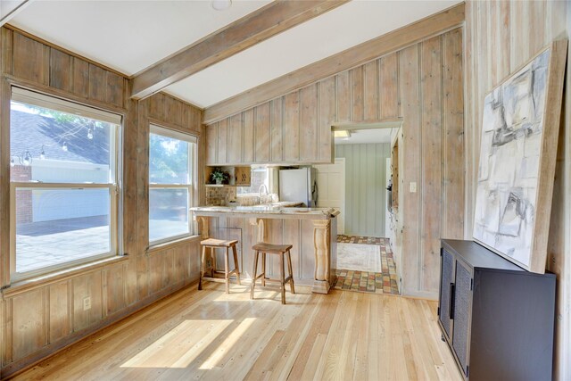 kitchen featuring light wood-type flooring, white fridge with ice dispenser, a breakfast bar area, wooden walls, and a peninsula