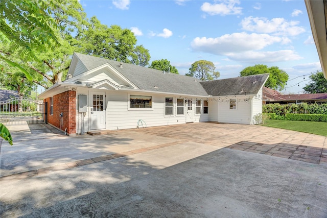 rear view of house with driveway, brick siding, and a shingled roof