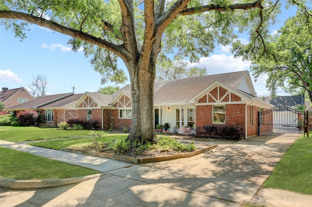 view of front of home featuring a gate, brick siding, driveway, and a front lawn