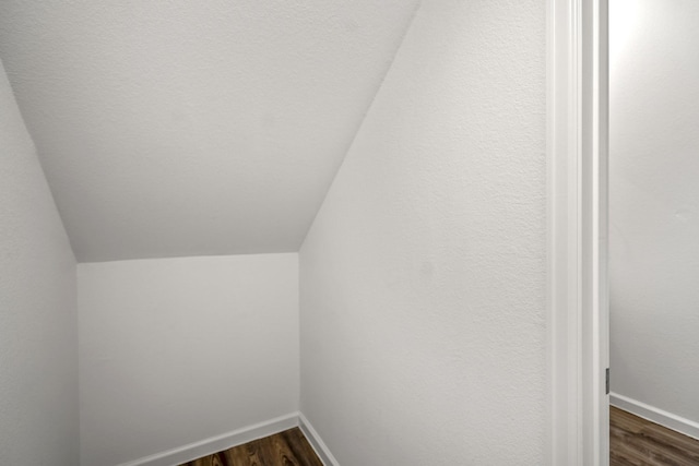 bonus room with dark wood-style floors, lofted ceiling, and baseboards