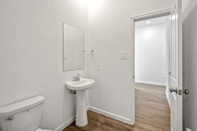 half bath featuring toilet, wood finished floors, baseboards, and a sink