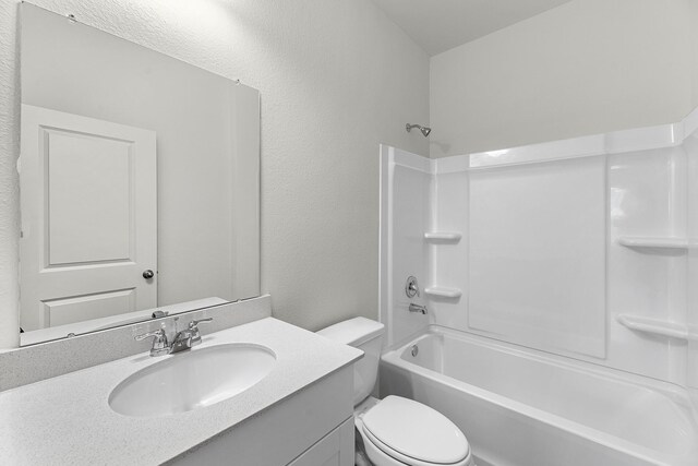 bathroom with toilet, vanity, a textured wall, and bathtub / shower combination