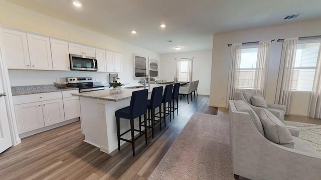 kitchen with appliances with stainless steel finishes, a kitchen island with sink, wood finished floors, white cabinets, and recessed lighting