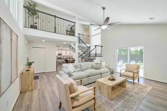 living room featuring a high ceiling, stairway, a ceiling fan, light wood-style flooring, and baseboards