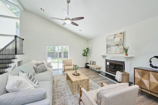 living area with a ceiling fan, wood finished floors, plenty of natural light, a glass covered fireplace, and high vaulted ceiling
