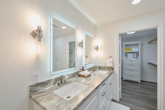 bathroom featuring double vanity, wood finished floors, a walk in closet, and a textured wall