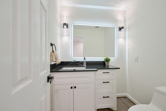 bathroom with vanity, toilet, wood finished floors, and baseboards