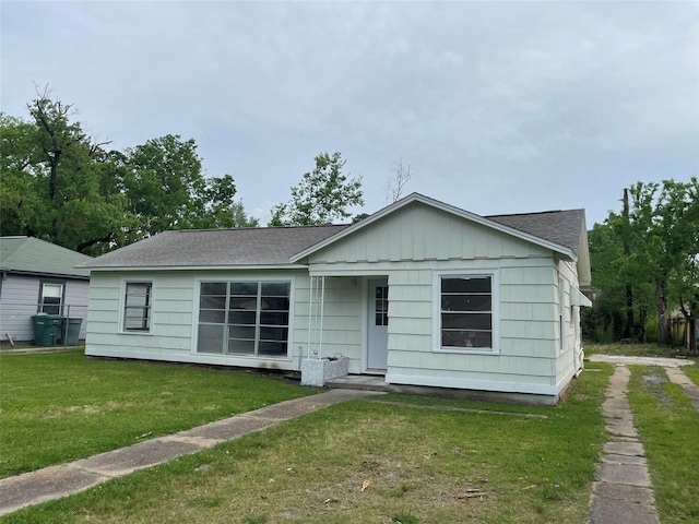 ranch-style home with a front lawn, roof with shingles, and board and batten siding