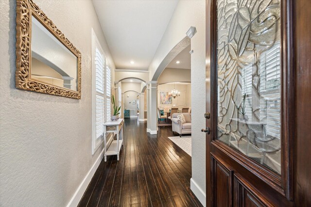 hallway with arched walkways, decorative columns, a textured wall, dark wood-type flooring, and baseboards