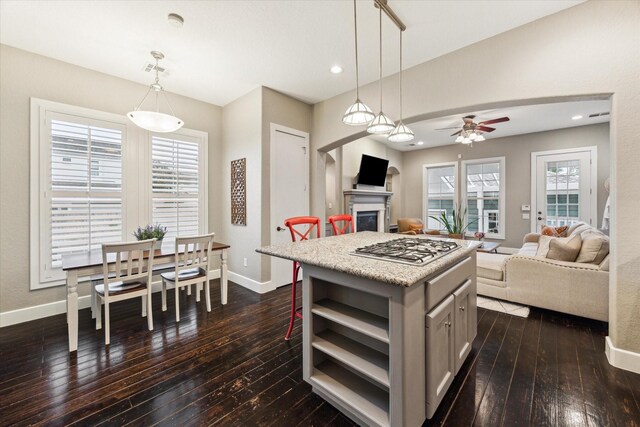 kitchen with open shelves, ceiling fan, dark wood finished floors, baseboards, and a glass covered fireplace