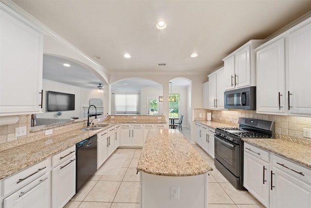 kitchen featuring black appliances, a sink, a kitchen island, arched walkways, and backsplash