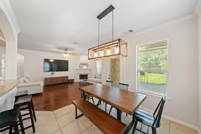 dining room featuring a ceiling fan, ornamental molding, a fireplace, light tile patterned floors, and baseboards