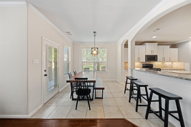 dining room featuring light tile patterned flooring, crown molding, arched walkways, and baseboards
