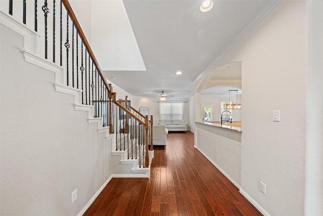 entrance foyer featuring ceiling fan, arched walkways, dark wood finished floors, stairway, and ornamental molding