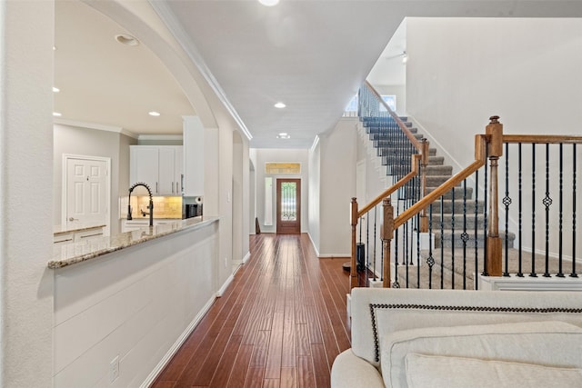 hallway with arched walkways, crown molding, stairs, baseboards, and dark wood finished floors