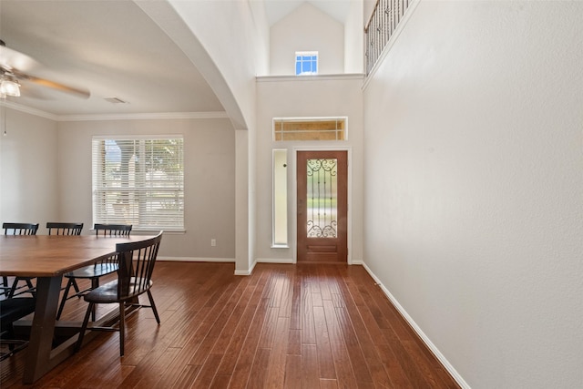 foyer entrance featuring ceiling fan, arched walkways, baseboards, dark wood-style flooring, and crown molding