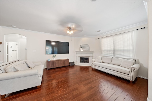 living room with ceiling fan, arched walkways, ornamental molding, dark wood-style floors, and a fireplace with raised hearth