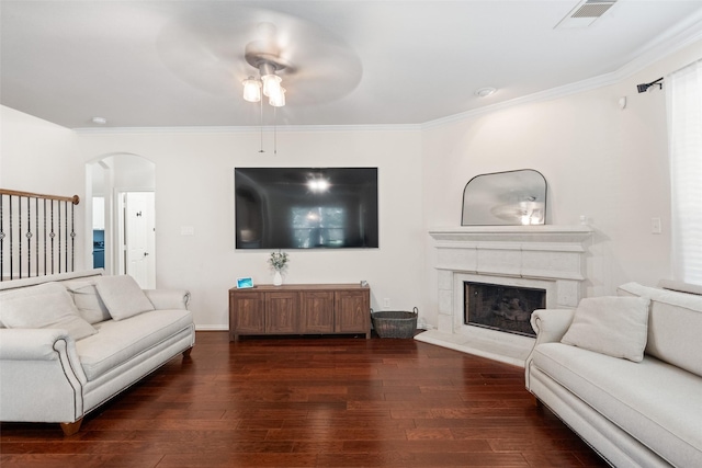 living room with arched walkways, hardwood / wood-style floors, ornamental molding, ceiling fan, and a premium fireplace