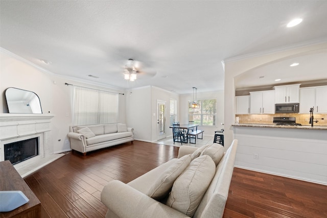 living area with dark wood-style floors, ornamental molding, a fireplace, a ceiling fan, and recessed lighting