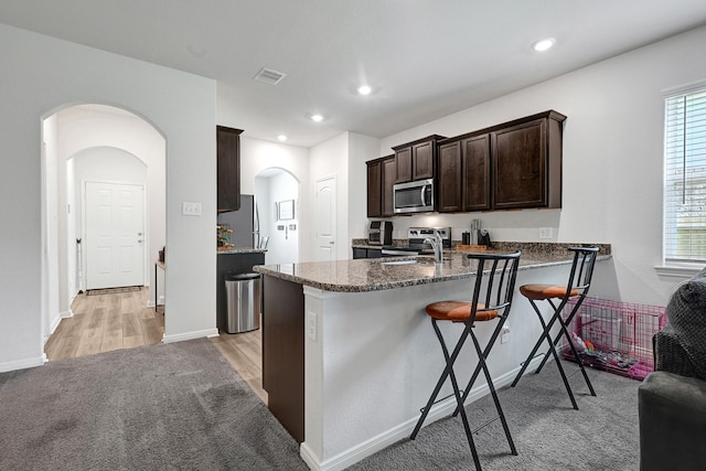 10707 Lost Maples Dr, Cleveland, TX 77328 - kitchen with stainless steel appliances, arched walkways, dark brown cabinetry, a kitchen bar, and a peninsula